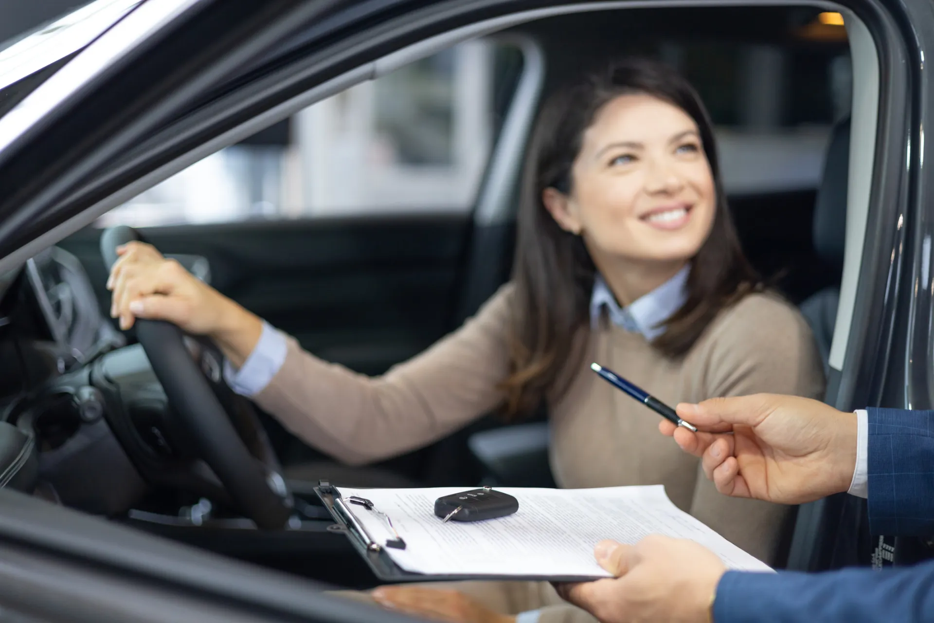 Szczęśliwa kobieta siedzi na miejscu kierowcy gotowa do podpisania umowy leasingu samochodu